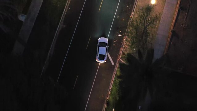 Aerial top down view of white car driving on the city streets at night.
