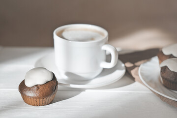 cup of latte coffee and fresh baked cupcakes with icing. chocolate muffins home baked in the morning. natural light.