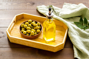 Bottle of olive cooking oil with green olives in bowl