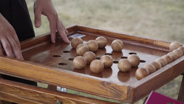 Unrecognizable couple is playing wooden game of nim outdoors. The man and woman take turns removing the wooden balls from the holes. Gameplay of ancient Chinese game.