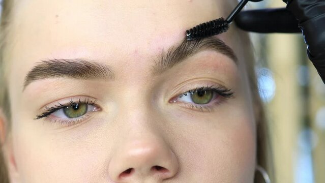 make-up artist combing and styling eyebrows after the procedure of correction and coloring of eyebrows
