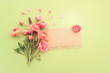 Top view image of pink flowers composition and empty note over green wooden background - obrazy, fototapety, plakaty