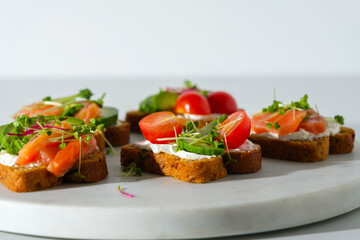 toasts with salmon, cherry, microgreens, open sandwich with fish on white marple board white background, healthy snack