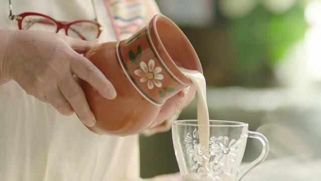 Pouring milk into the glass from crock in the country