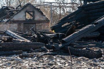 A wooden house in the village burned down because of a forest fire. Charred boards and various things lie on the ground, covered with ash and smoke.