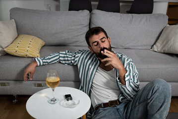 Alcoholic man holding a cigarette with alcohol drink in the glass on the table and smoking...