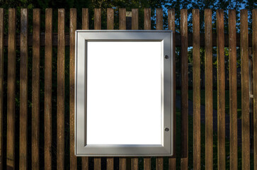 Blank white mockup template of a lockable metal poster frame on a wooden fence wall. Background...
