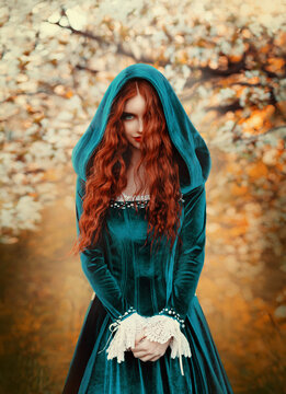 Portrait mystical fantasy red-haired woman witch looking at camera. Girl princess. Blue green medieval Victorian dress. Glamorous lady queen, red long curly hair waving flying in wind. Autumn forest.