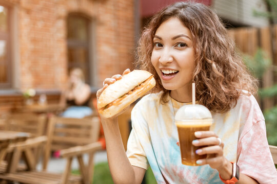 a girl eats a burger or a hot dog in a fast food cafe and a sweet coffee drink