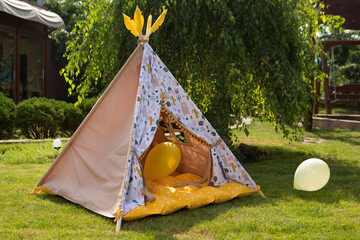 empty tepee-like children's tent outdoors, surrounded by balloons