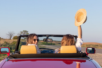 Back view of young girls on a red classic cabrio car looking at camera enjoying the summer girls...