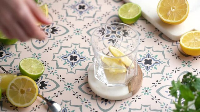 Cocktail lemonade preparation: female hand adding lemon slices to a glass, pressing on them with a muddler on a multicolored portugal tiles background. Slow motion