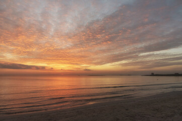 Fototapeta premium Tramonto sul mare con riflessi del sole sull'acqua e sulla sabbia.