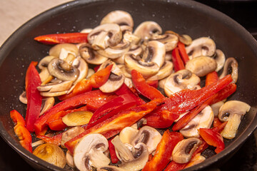 Overhead shot of mushrooms, red onions and red and yellow bell peppers frying in a pan with old wooden spatula
