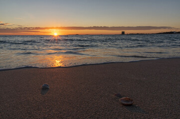 Tramonto sul mare con riflesso del sole sull'acqua e sulla sabbia.