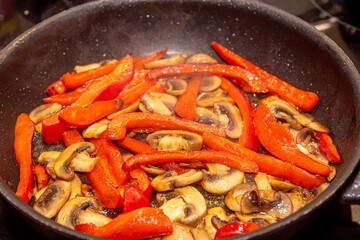 Overhead shot of mushrooms, red onions and red and yellow bell peppers frying in a pan with old wooden spatula