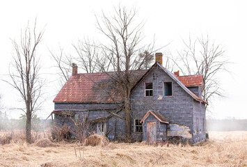 An old abandoned spooky looking farmhouse in winter on a farm yard in rural Ontario, Canada