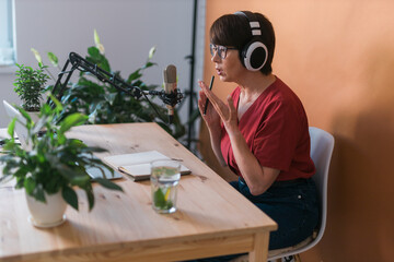 Portrait of mature woman wearing headphones and talking at online radio station - podcast and...