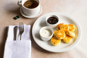Cottage cheese pancakes, syrniki, ricotta fritters on white ceramic plate with sour cream and jam. Healthy and delicious morning breakfast. Beige background. Food for kids