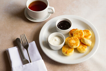 Cottage cheese pancakes, syrniki, ricotta fritters on white ceramic plate with sour cream and jam. Healthy and delicious morning breakfast. Beige background. Food for kids