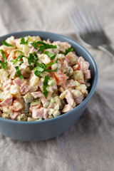 Homemade Olivier salad in a Bowl on a white wooden background, side view.