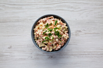 Homemade Olivier salad in a Bowl on a white wooden background, top view. Flat lay, overhead, from above.