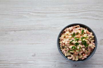 Homemade Olivier salad in a Bowl on a white wooden background, top view. Flat lay, overhead, from above. Space for text.