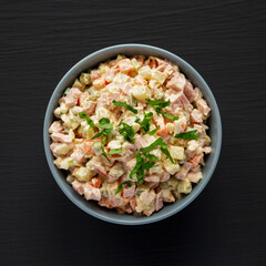 Homemade Olivier salad in a Bowl on a black wooden background, top view. Flat lay, overhead, from above.