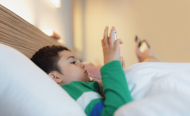 Happy Kid lying in bed holding tablet watching cartoon and chatting with friends on digital pad, Cute young boy playing games online on internet, Child relaxing at home with family