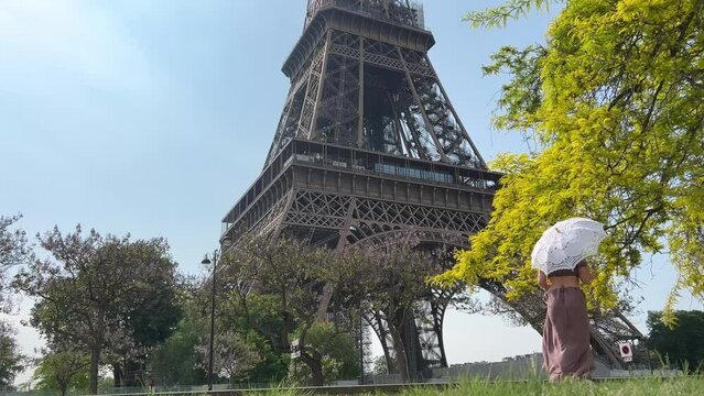girl in a long dress with an openwork umbrella goes to the eiffel tower with her back to the camera can be used for advertising text for the interior very beautiful slow motion video. High quality 4k