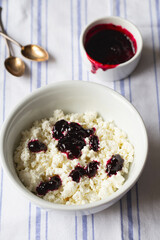 Homemade cottage cheese in a deep plate. Milk product. Granular cottage cheese with black currant jam