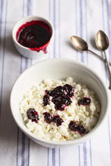 Homemade cottage cheese in a deep plate. Milk product. Granular cottage cheese with currant jam. Healthy breakfast.