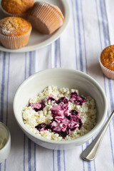 Homemade cottage cheese in a deep plate. Milk product. Granular cottage cheese with black currant jam