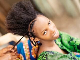Young afro beauty smiling and being braided, eighteen years old