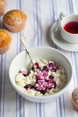Homemade cottage cheese in a deep plate. Milk product. Granular cottage cheese with black currant jam