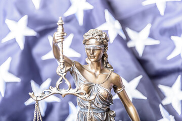The statue of justice Themis or Iustitia, the goddess of justice blindfolded against a flag of the United States of America, as a legal concept.