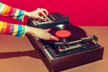 Colorful image of female hands spinning retro vinyl record player like a dj isolated over red background