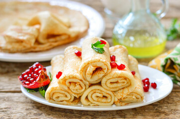 Thin pancakes (bliny). Pancakes rolled into tubes on a white plate. Wooden background.