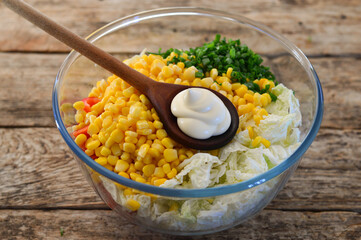 Salad with canned corn and vegetables. Glass bowl of loy lettuce. Wooden background.