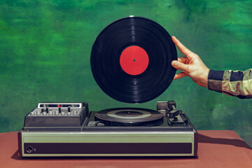 Colorful image of male hand holding retro vinyl record in front of vintage player isolated over...