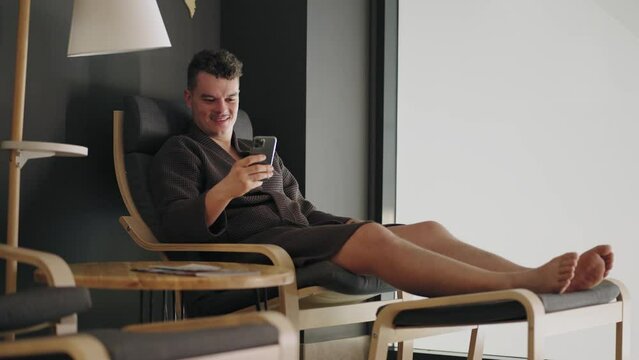adult wealthy man is resting in spa salon or health center, sitting in lounger and using smartphone, viewing positive news