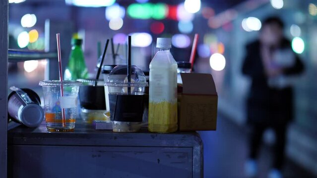 Disposable plastic cups and bottles are left on street of Seoul. Close-up shot of trash with blurred sidewalk in background, evening time. People snack and drink on the go, and then just leave package