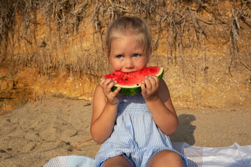 little cute girl eating watermelon sitting on the beach at sunset