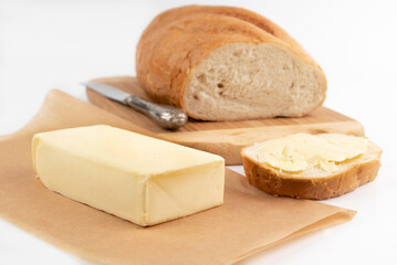 On a light background on the board is light bread, butter, a knife and a piece of bread, buttered.