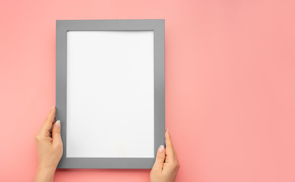 Hanging a photo frame mockup on pink wall. Picture frame mockup. Holding frame mockup. Photo Mockup. Female hands hold frame with white paper. copy space