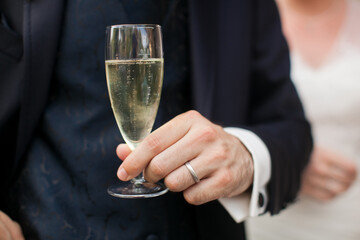 Close up photo of a groom's hand in an elegant wedding suit with a glass of sparkling wine