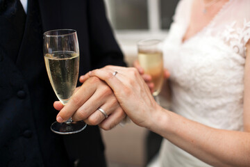 Close up photo of a groom and bride hands in an elegant wedding suit and dress with a glasses of sparkling wine
