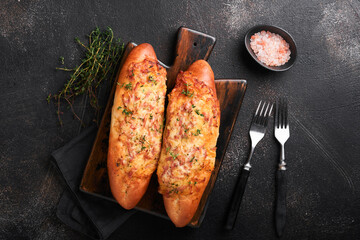 Baguette boats. Hot baked sandwich on baguette bread with ham, bacon, vegetables and cheese on parchment and black dark concrete background. Top view. Copy space.