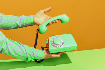 Colorful bright image of male hand picking up handset of old-fashioned green colored phone isolated over orange background