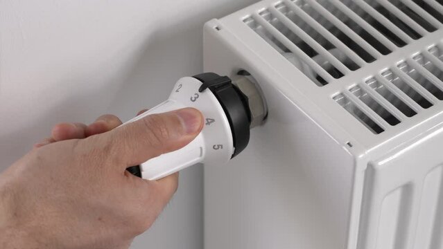A man sets a white thermostat with his hand to adjust the central heating radiator to the average economical mode of maintaining the temperature in the room